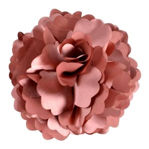 Puede incluir: Una gran flor de tela rosa claro con un diseño de volantes y capas. La flor está hecha de un material suave y sedoso y tiene un aspecto delicado y femenino.