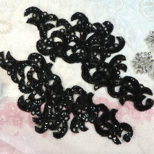 Könnte beinhalten: Zwei schwarze Spitzenapplikationen mit Pailletten. Die Applikationen sind im Blumendesign gehalten und eignen sich perfekt, um jedem Projekt einen Hauch von Eleganz zu verleihen.