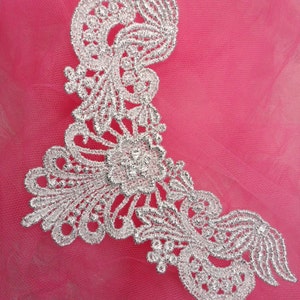 May include: Silver lace trim with a floral design on a pink background.