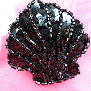 May include: A black sequined seashell applique. The shell is made of small black sequins and beads, and is shaped like a scallop shell.