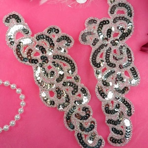 Puede incluir: Dos apliques de lentejuelas plateadas en un diseño floral sobre un fondo rosa.