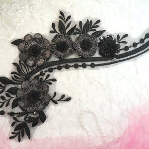 Peut inclure: Applique en dentelle florale noire avec des accents perlés. L'applique présente un design incurvé avec plusieurs fleurs et feuilles noires.