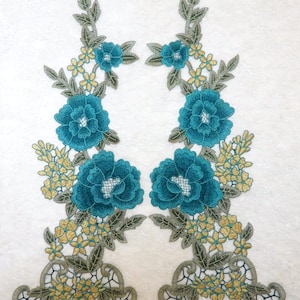 May include: Two teal blue floral appliques with green leaves and yellow flowers. The appliques are perfect for adding a touch of elegance to clothing, crafts, or home decor.