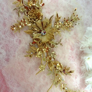 Peut inclure: Applique florale dorée avec des paillettes et des perles. L'applique présente une grande fleur avec des fleurs et des feuilles plus petites. L'applique est parfaite pour ajouter une touche d'élégance à tout projet.