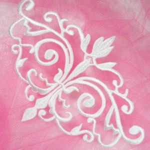 Puede incluir: Aplique de encaje blanco bordado con un diseño floral sobre un fondo rosa.