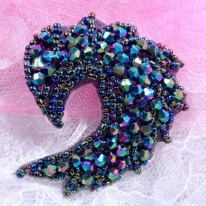 May include: A dark blue and iridescent beaded brooch in the shape of a crescent moon. The brooch is made of small, faceted beads that catch the light and sparkle.