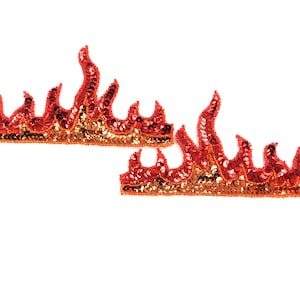 Pode incluir: Duas aplicações em forma de chama, cada uma com lantejoulas vermelhas e douradas. As aplicações estão dispostas sobre um fundo branco. As lantejoulas são costuradas em um suporte de malha, criando um efeito brilhante. Estas aplicações são adequadas para a ornamentação de roupas.