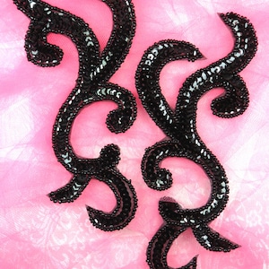 May include: Two black sequined embellishments in a floral design on a pink fabric background.