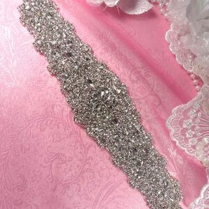 May include: A silver rhinestone bridal sash with a delicate, intricate design. The sash is perfect for adding a touch of sparkle to a wedding dress.