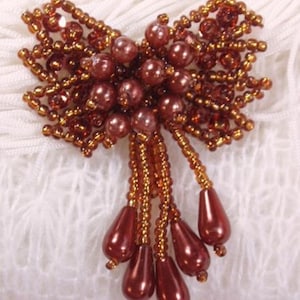 May include: A brown beaded bow with a cluster of brown pearlescent beads in the center and a dangling fringe of brown pearlescent beads.