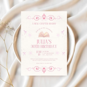 Pode incluir: Um cartão de convite rosa claro com o texto "Um novo capítulo começa!" e "30º aniversário de Julia". O cartão inclui redemoinhos decorativos, corações e estrelas. O convite está em um prato branco e um fundo de tecido branco.