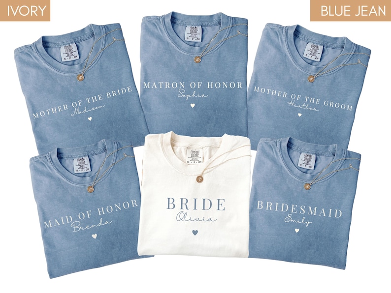 K&ouml;nnte beinhalten: Eine Auswahl an Jeansblauen und elfenbeinfarbenen T-Shirts mit goldenen Halsketten. Die Shirts sind mit Hochzeitsbezeichnungen wie "Mother of the Bride" und "Bridesmaid" sowie Namen bedruckt. Das elfenbeinfarbene Shirt tr&auml;gt die Aufschrift "Bride".