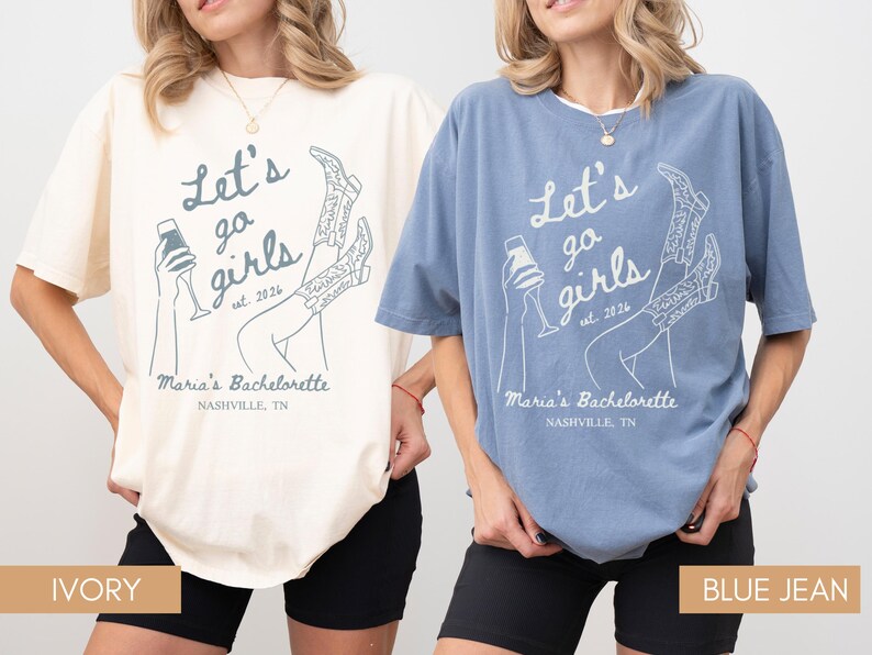 May include: Two t-shirts, one ivory and one blue jean, with the text "Let's go girls" and "Maria's Bachelorette Nashville, TN" printed on them. The design includes a champagne glass and cowboy boots. The shirts are a relaxed fit.