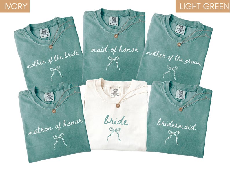 May include: A selection of light green and ivory t-shirts with wedding-related text. The shirts are printed with "mother of the bride," "maid of honour," "mother of the groom," "matron of honour," "bride," and "bridesmaid." Each shirt has a bow graphic.
