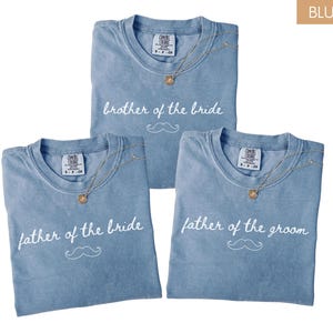 May include: Three blue jean-coloured t-shirts with white text and a moustache graphic. The shirts say "brother of the bride", "father of the bride", and "father of the groom". Each shirt has a gold necklace.