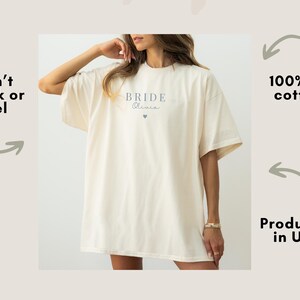 K&ouml;nnte beinhalten: Cremefarbenes &uuml;bergro&szlig;es T-Shirt mit dem Wort "Bride" und dem Namen "Olivia" in zarter Schrift sowie einem kleinen Herz aufgedruckt. Das Shirt besteht aus 100 % US-Baumwolle.