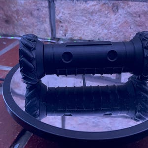 May include: A black robot with two wheels on each side, the wheels have a textured tread pattern. The robot is sitting on a black circular platform.