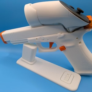 May include: A white and orange VR headset controller mounted on a white gun-shaped stand. The stand has the word "GLOCK" embossed on it. The controller has black buttons and orange accents. The background is a solid blue.