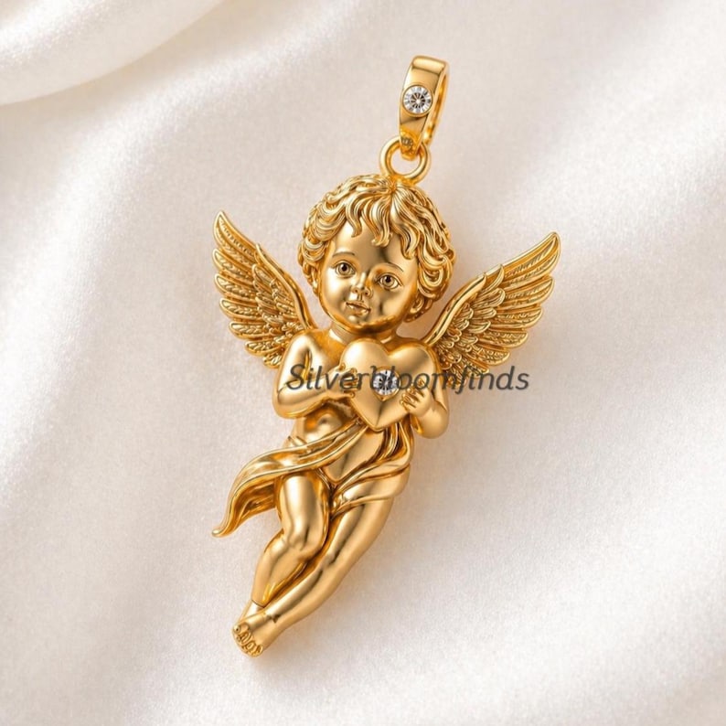 May include: A gold-colored pendant in the shape of a cherub holding a heart. The cherub has detailed wings and curly hair. The pendant has a small gemstone at the top and the text "Silverbloomfinds" is visible.