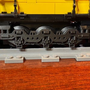 Puede incluir: Primer plano de una locomotora de tren de juguete negra con cuatro ruedas y un cuerpo amarillo. El tren está en una vía gris.