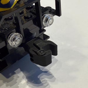 Puede incluir: Primer plano de un acoplamiento de tren LEGO de plástico negro con una luz de plástico transparente en el lateral.