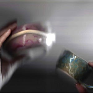 Könnte beinhalten: Verschwommenes Bild einer Person, die eine transparente Schüssel mit rosa Inhalt und einen Keramikbecher mit blau-grüner Marmorierung hält. Der Becher hat einen Henkel und wird in der anderen Hand gehalten.