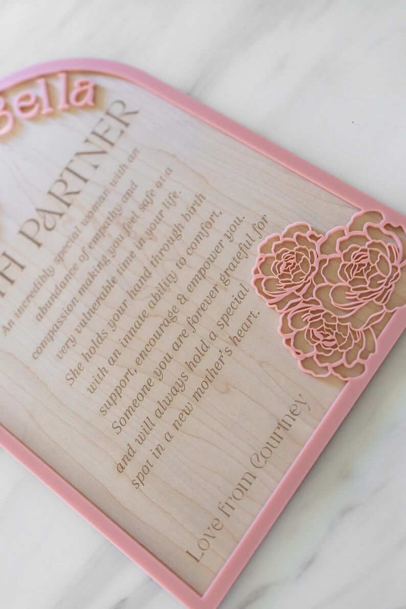 Puede incluir: Una placa de madera arqueada con un borde rosa que presenta el nombre Bella en letras rosas en relieve. El texto dice: An incredibly special woman with an abundance of empathy and compassion making you feel safe at a very vulnerable time in your life.