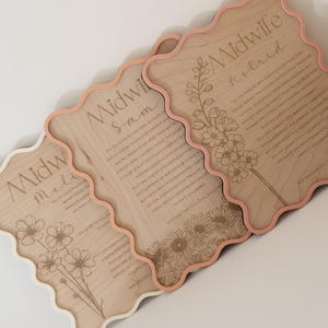 May include: Three scalloped-edge wooden plaques with engraved text and floral illustrations. Each plaque features the word Midwife followed by a name, Sam, Meli, or Astrid, and a paragraph of text expressing gratitude, finished with a coloured border.