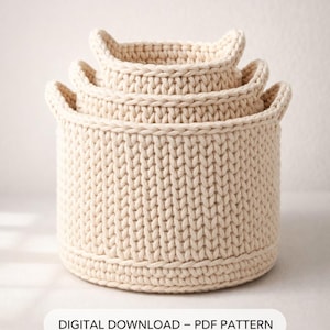 May include: Three cream-colored, crocheted baskets of varying sizes are stacked together. Each basket has a rounded shape with two small handles. The text "DIGITAL DOWNLOAD - PDF PATTERN" is displayed at the bottom.