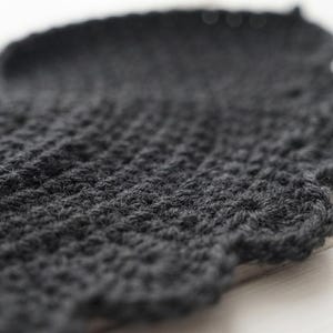 May include: A dark charcoal gray crocheted textile piece featuring a dense, textured stitch pattern throughout the main body and a decorative, scalloped edge finish along the curved border, showcasing the intricate yarn loops and construction.