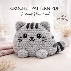 May include: A gray crocheted cat with black stripes and facial details. The cat has large black eyes and a small black nose. The text "CROCHET PATTERN PDF Instant Download" is at the top of the image, with "EASY PATTERN" in a circle on the right.