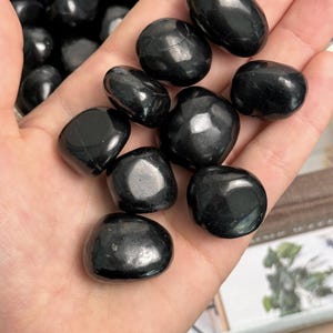 May include: A collection of black tumbled stones. The stones are smooth and polished, with a glossy finish.