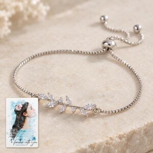 Close view of the bracelet's asymmetric silver-tone twig with clear marquise leaves, tiny buds and fine box chain. A personalized digital greeting card is shown alongside.