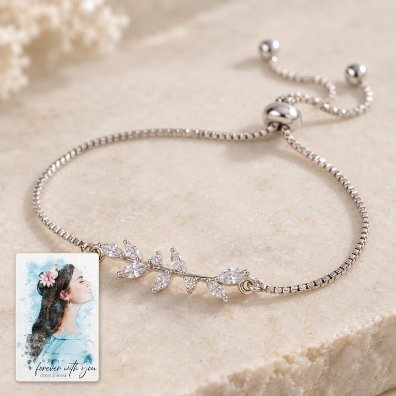 Close view of the bracelet's asymmetric silver-tone twig with clear marquise leaves, tiny buds and fine box chain. A personalized digital greeting card is shown alongside.