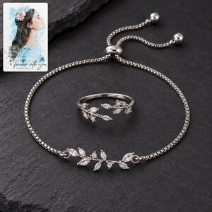 Clear leaf-accent bracelet and matching ring on charcoal slate, showing the polished slider and two ball-ended chain tails. A personalized digital greeting card is shown alongside.