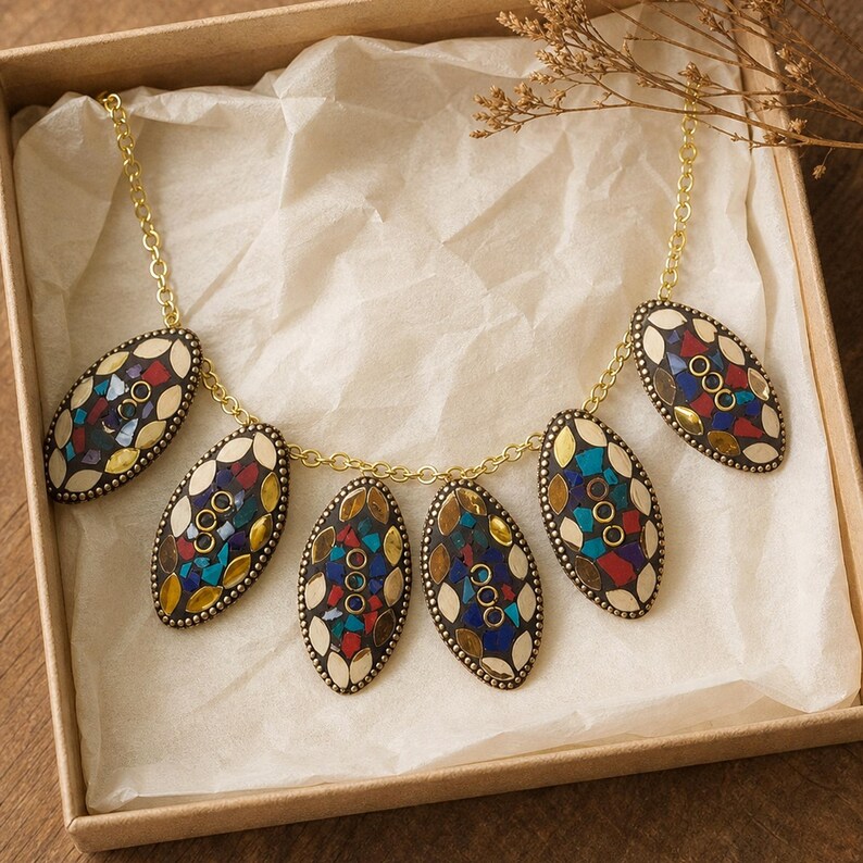 May include: A necklace featuring five oval-shaped pendants connected by a gold-toned metal chain. Each pendant displays a mosaic pattern of inlaid colorful stone fragments in shades of red, blue, and yellow, bordered by cream-colored accents.