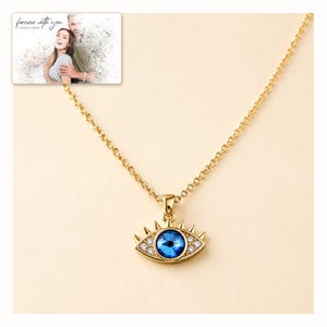 Gold-tone necklace with a blue eye-shaped pendant, catalog view. A personalized greeting-card example appears in the corner.