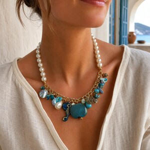 May include: A necklace featuring a strand of white pearls connected to a gold-tone chain. The chain is adorned with various charms, including blue ceramic pieces, a seahorse, and iridescent shell-like beads, creating a coastal-inspired design.