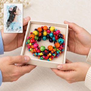 Rainbow Bead Bracelet shown during a believable gift-giving moment between adults with the jewelry visible. A personalized digital greeting card is shown alongside.