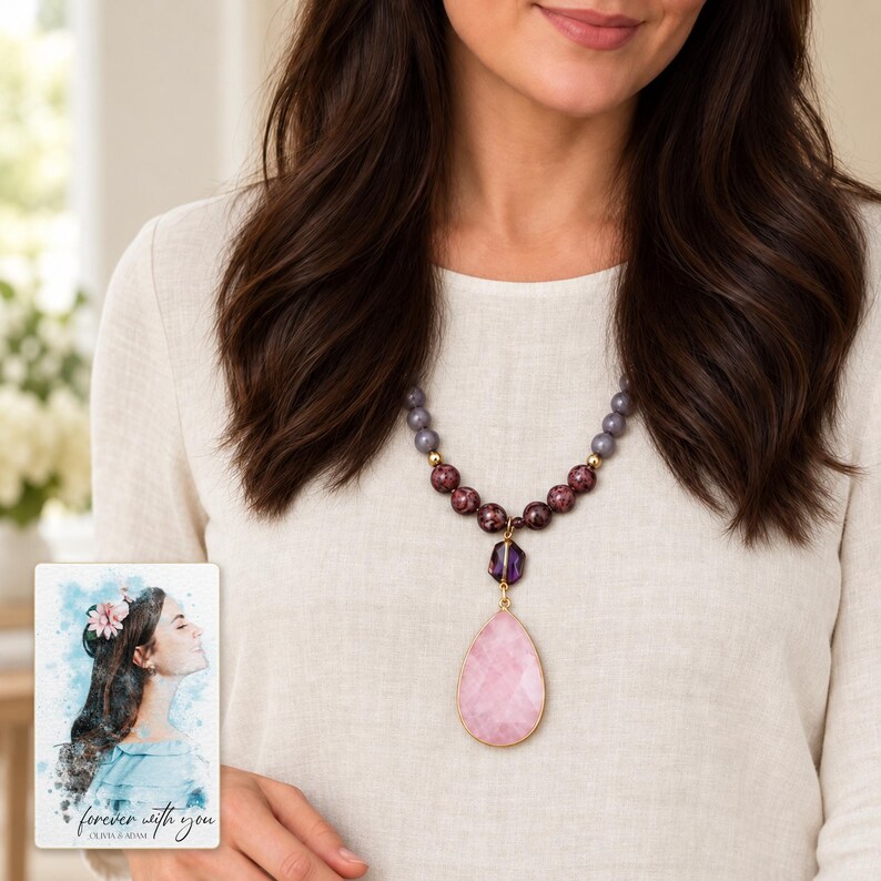 Close adult torso view of the long pink pendant necklace over ivory linen, showing the lower burgundy and smoky-grey bead groups. A personalized digital greeting card is shown alongside.