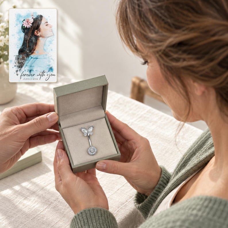 Adult recipient looking down at the butterfly navel bar in an open box held close to a linen-covered table. A personalized digital greeting card is shown alongside.
