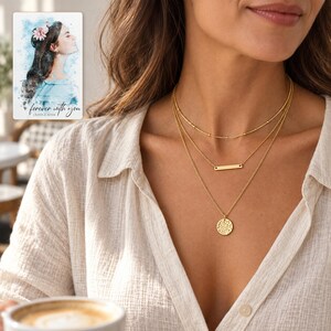 Adult woman wearing the complete three-layer gold-tone necklace with a linen blouse in a daylight cafe. A personalized digital greeting card is shown alongside.