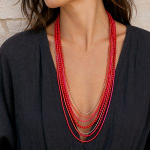 Long multistrand scarlet red pink and silver necklace worn with an ivory linen top in warm natural window light