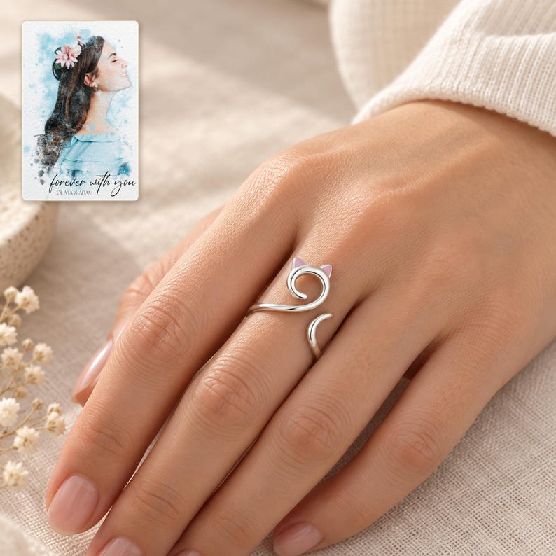 Adult woman wearing the pink-ear cat-curl ring on her ring finger with a cream sleeve. A personalized digital greeting card is shown alongside.