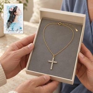 Two adults exchange an open jewelry box with the exact gold-tone cross necklace visible inside. A personalized digital greeting card is shown alongside.
