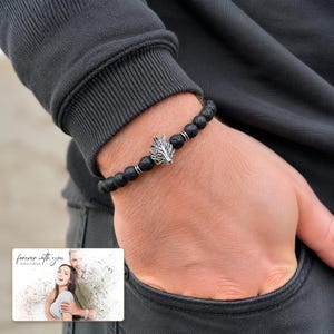 Black bead bracelet with silver-tone wolf-head detail, worn view. A personalized greeting-card example appears in the corner.
