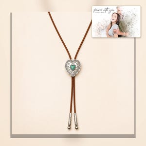Brown cord bolo necklace with a silver-tone heart slide and turquoise-color center, framed product view. A personalized greeting-card example appears in the corner.
