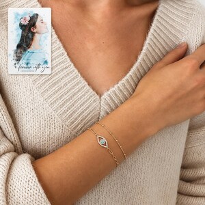 Gold Tone Evil Eye Bracelet Duo worn by an adult model for styling and everyday styling. A personalized digital greeting card is shown alongside.