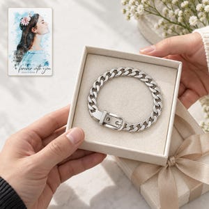 Adult hands passing an open ivory box containing the closed silver tone belt buckle bracelet. A personalized digital greeting card is shown alongside.