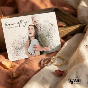 May include: A greeting card with the words "forever with you" and the names Olivia & Adam. The card features a photo of a couple. Two textured rings, one silver and one gold, are next to the card. The background is a soft, neutral color.